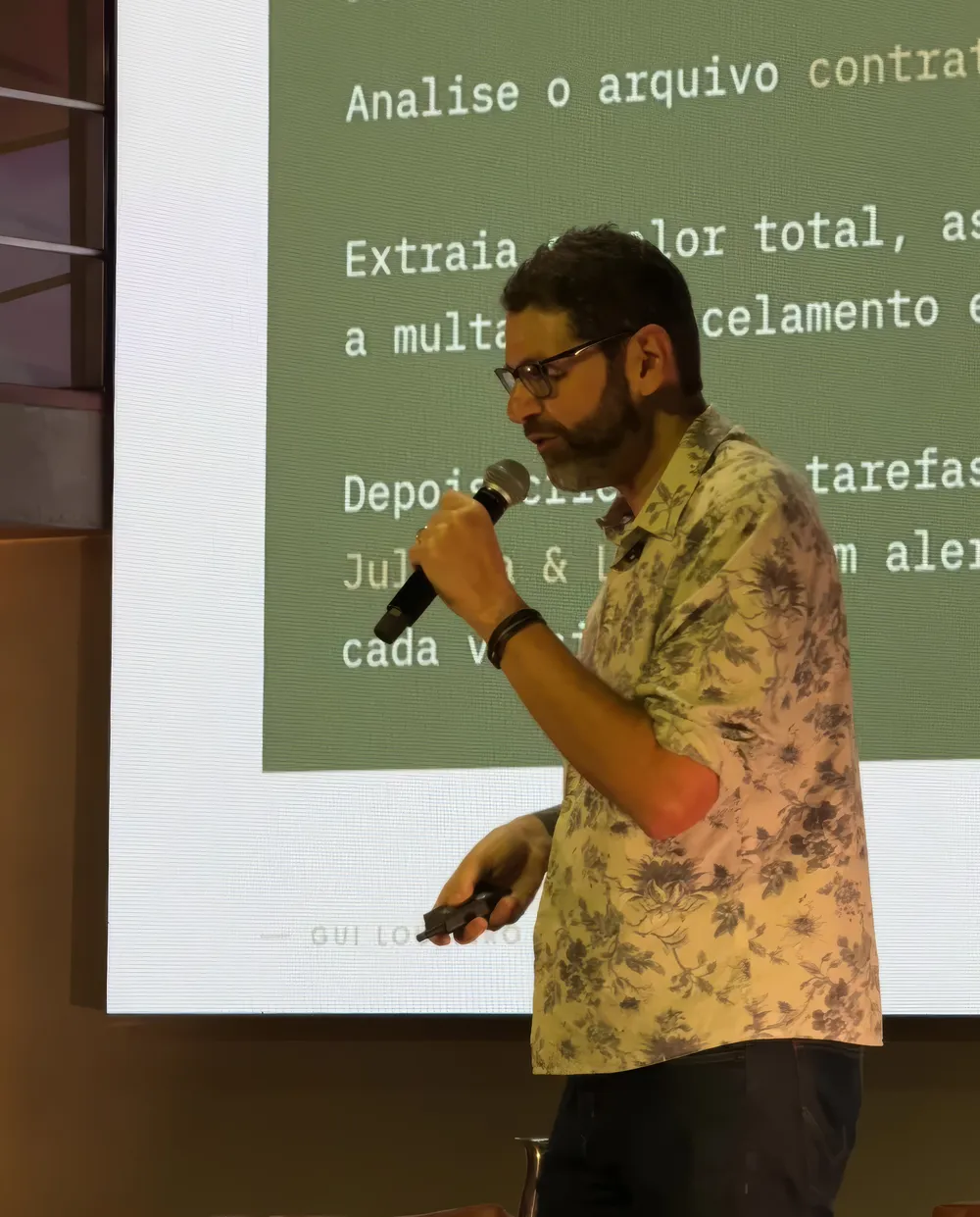 Gui Loureiro no palco, de microfone, diante de um slide do Claude Code